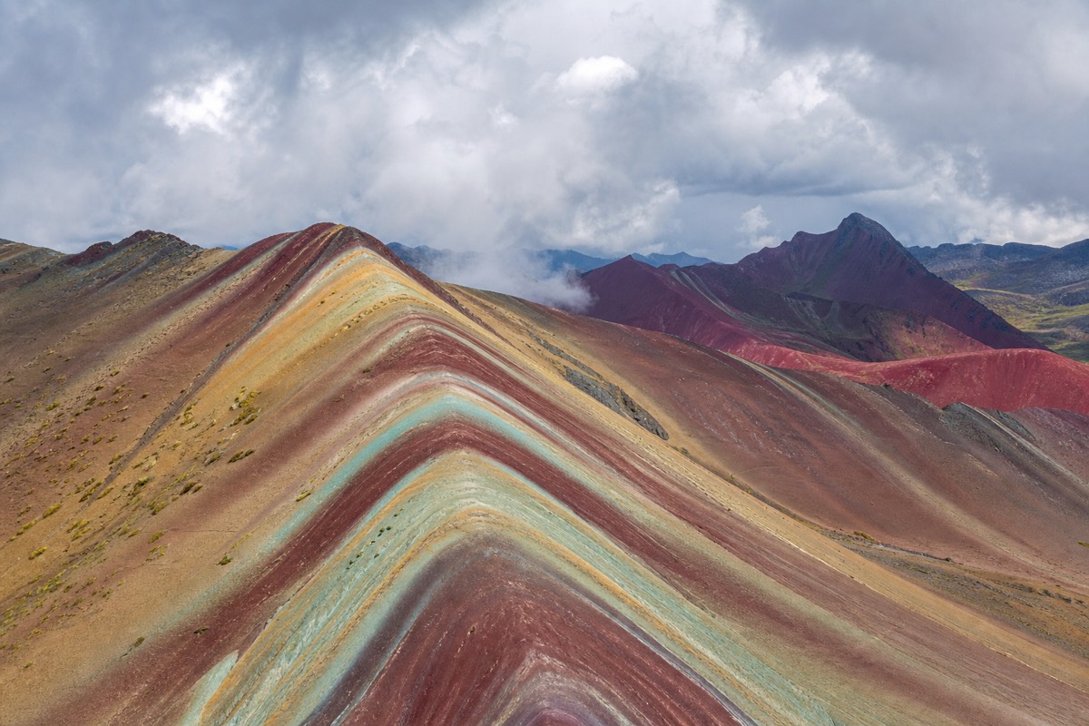 Hikers on the striped mineral ridges of Vinicunca Rainbow Mountain with the snow-capped Vilcanota range behind